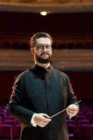 Młody dyrygent Jan Stańczyk pozuje do zdjęcia trzymając w rękach batutę